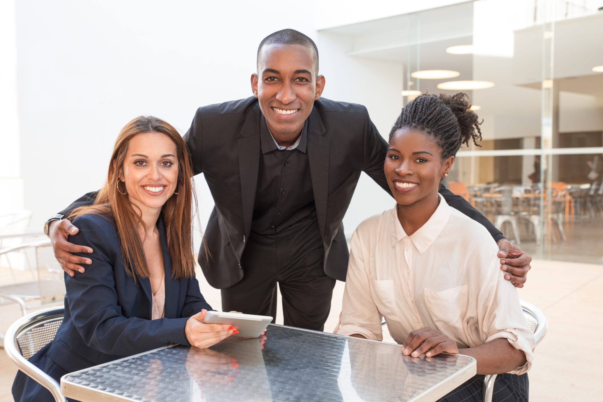 Happy African American businessman embracing female colleagues at cafe. Portrait of three business colleagues sitting at cafe. Successful team concept