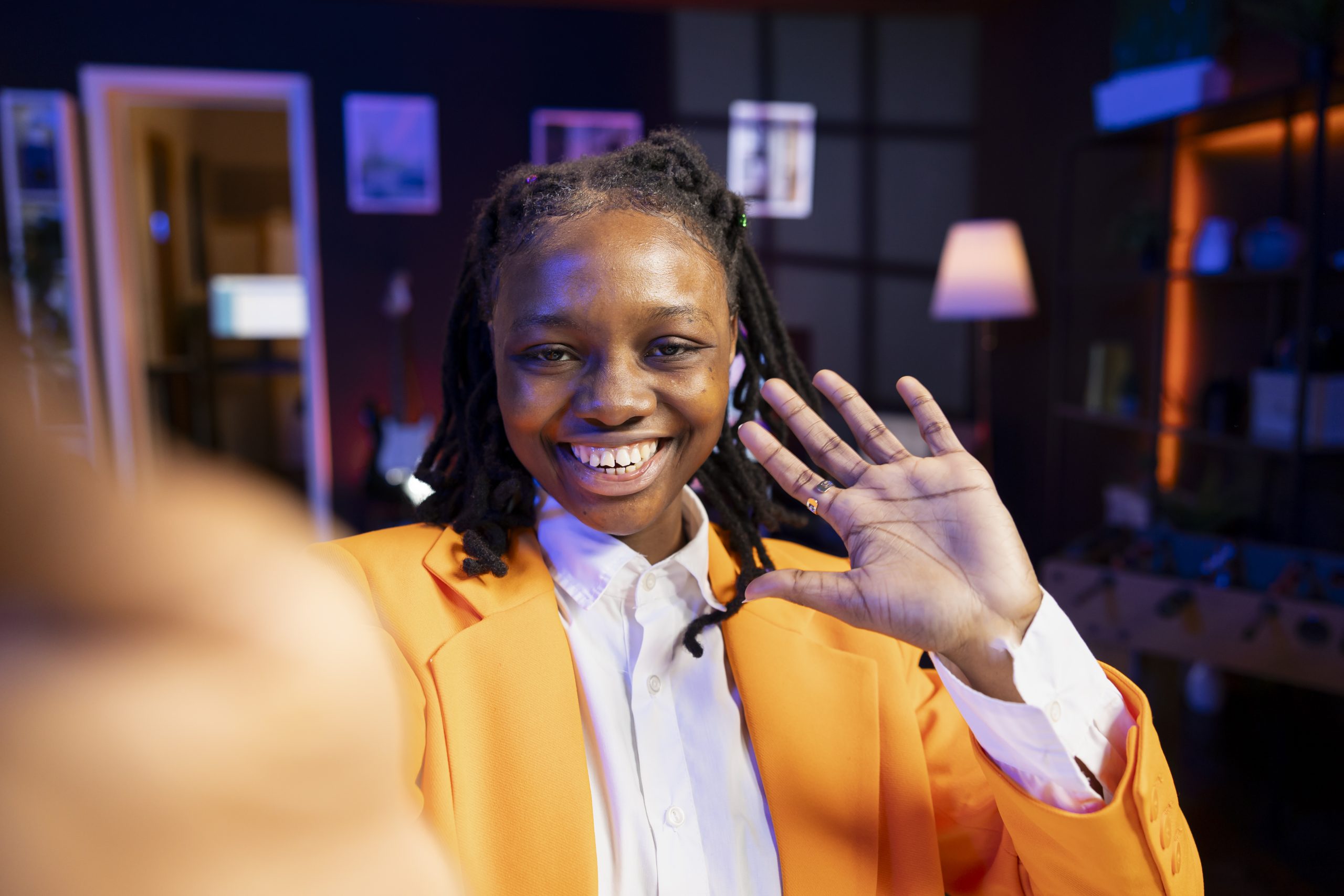 Joyful Gen Z girl records introductory video with smartphone, inviting viewers to subscribe to channel. Upbeat internet star uses selfie camera to film herself connecting with fans